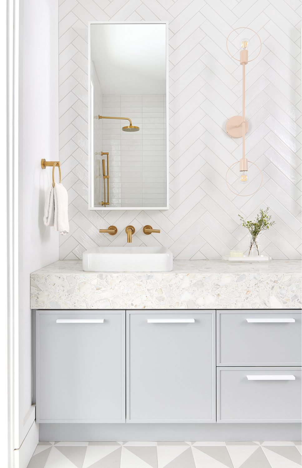 A powder room with a marble vanity, brass taps and a herringbone marble wall