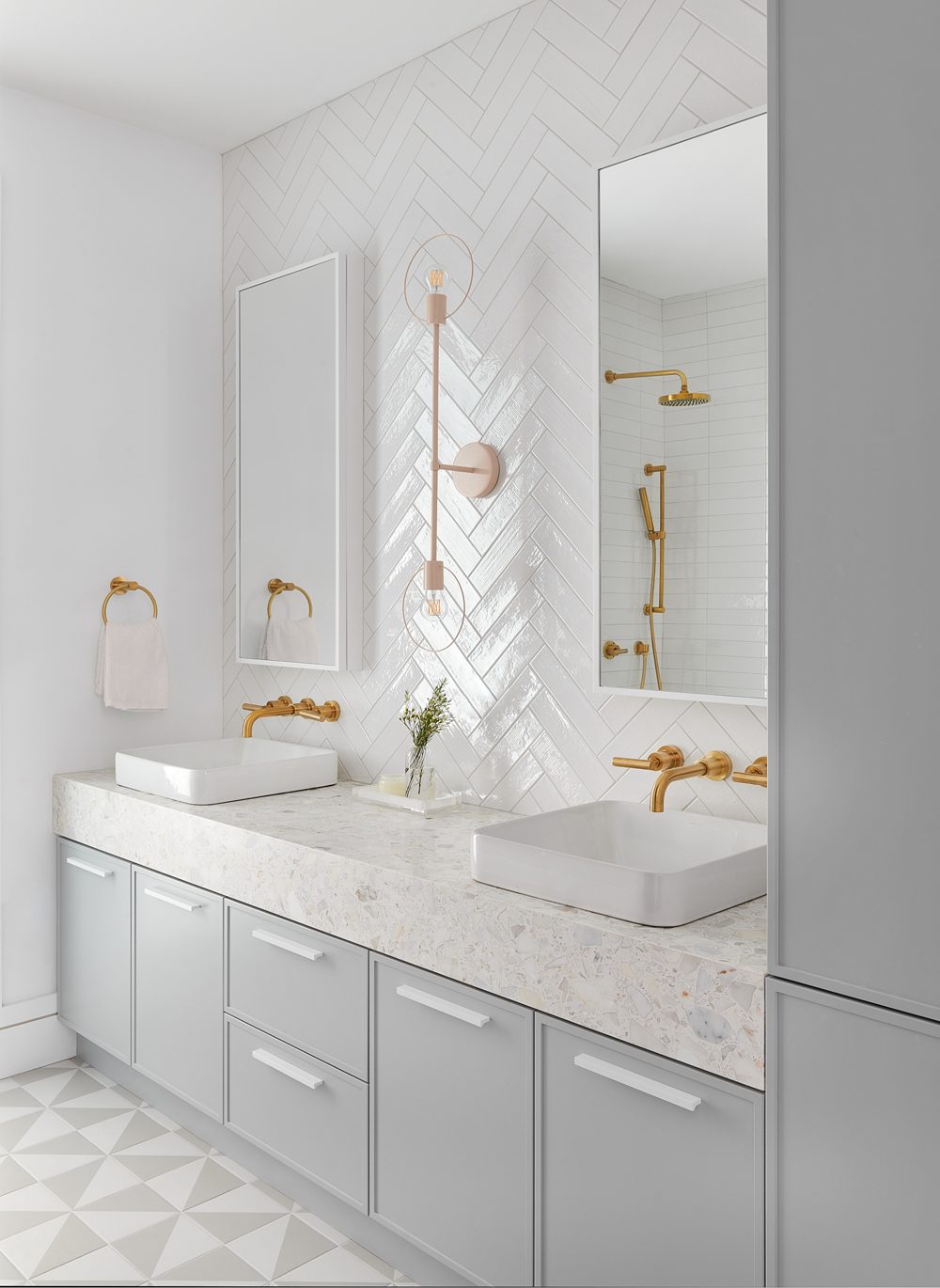 An ensuite with a grey double vanity, brass fittings and a patterned marble floor