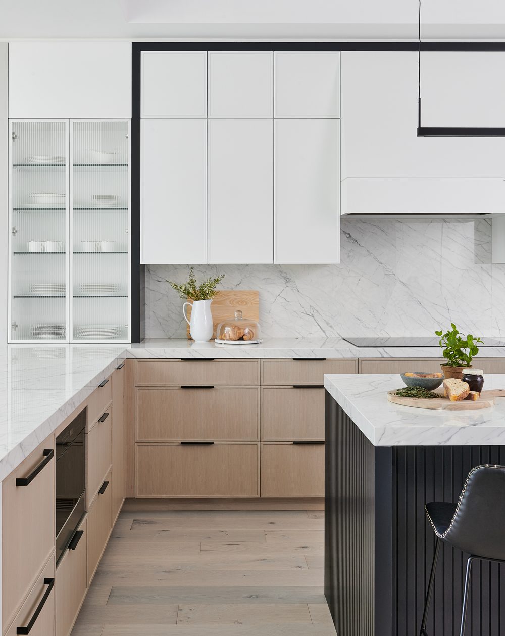 A kitchen with white-oak lower cabinets, white uppers and a black-framed island