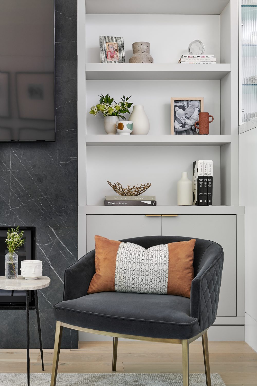 A reading corner with a black marble fireplace edge, built-in shelves and a velvet chair