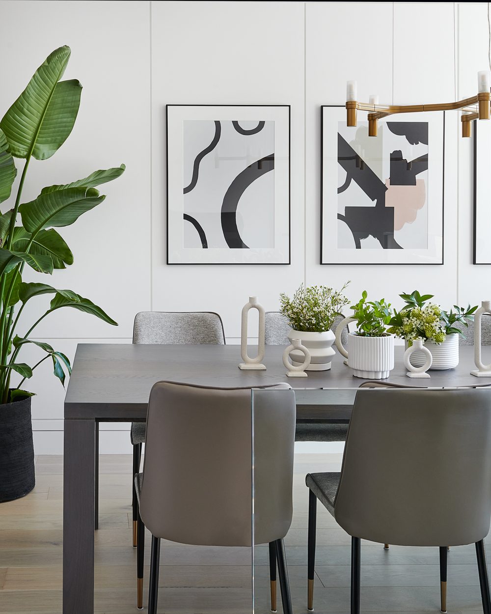 A dining room with grey chairs, a tall plant and two abstract prints