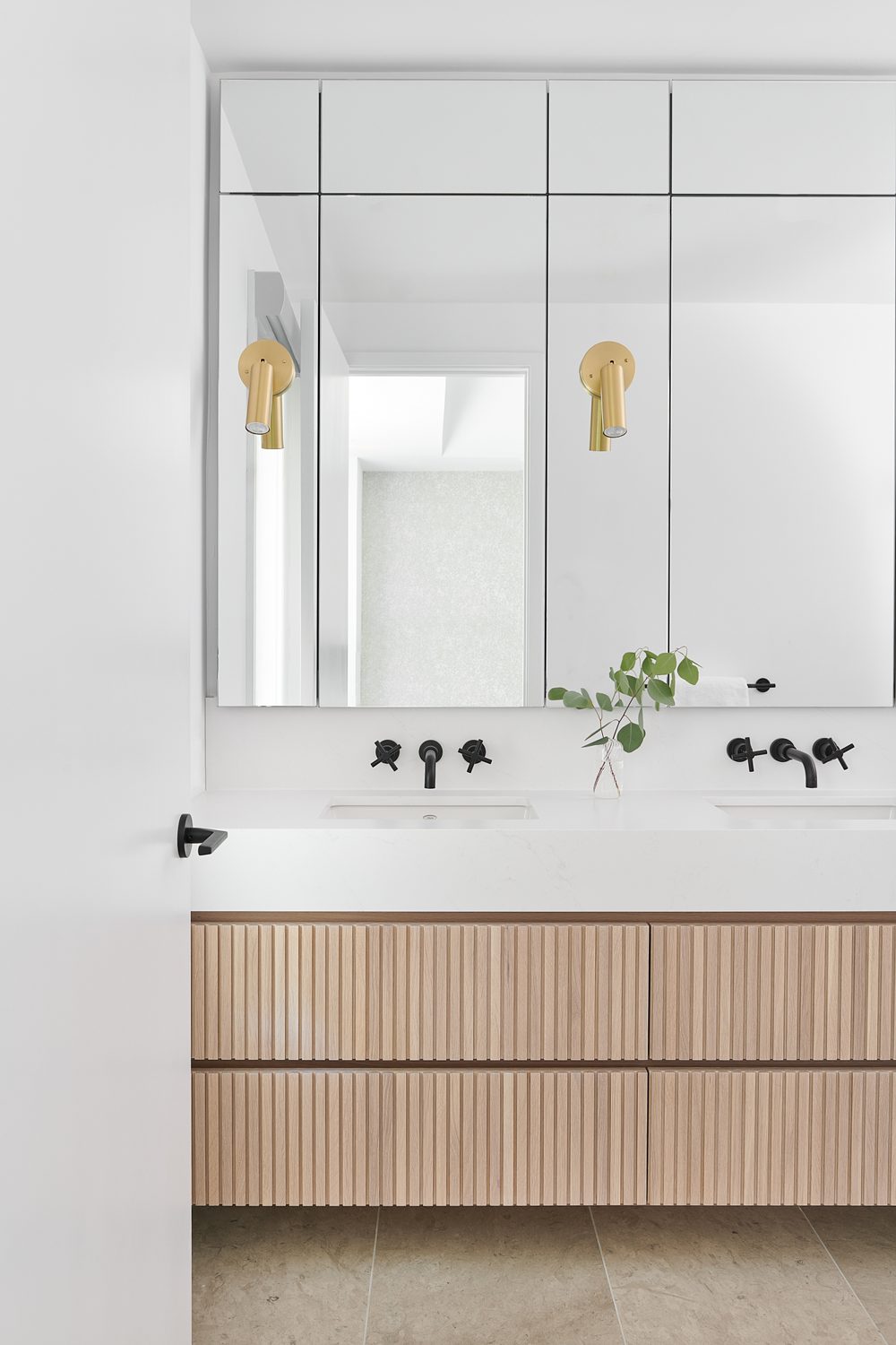 A fluted oak vanity with black taps and a mirrored wall