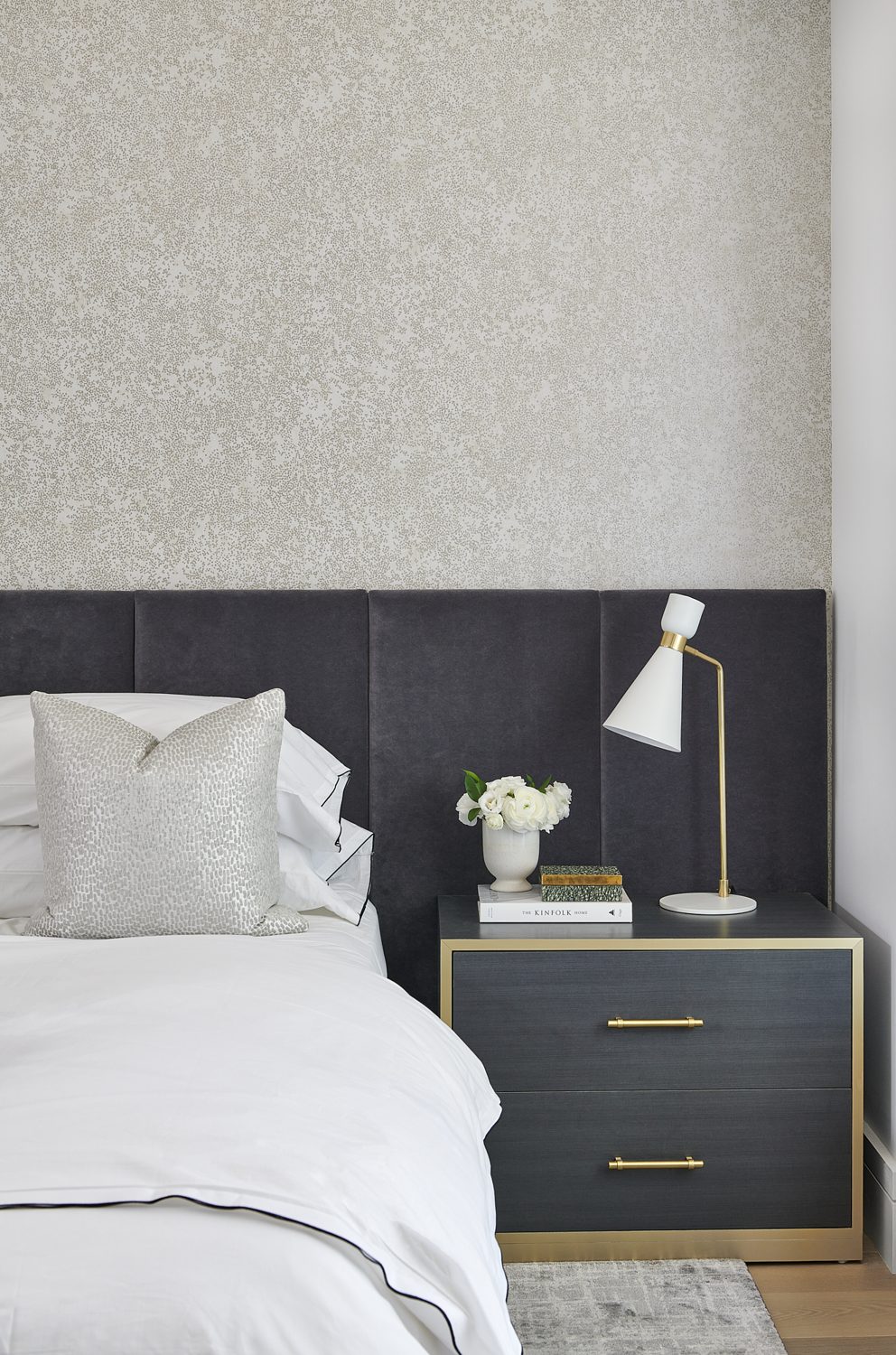 A charcoal channel headboard with white linen and a brass lamp