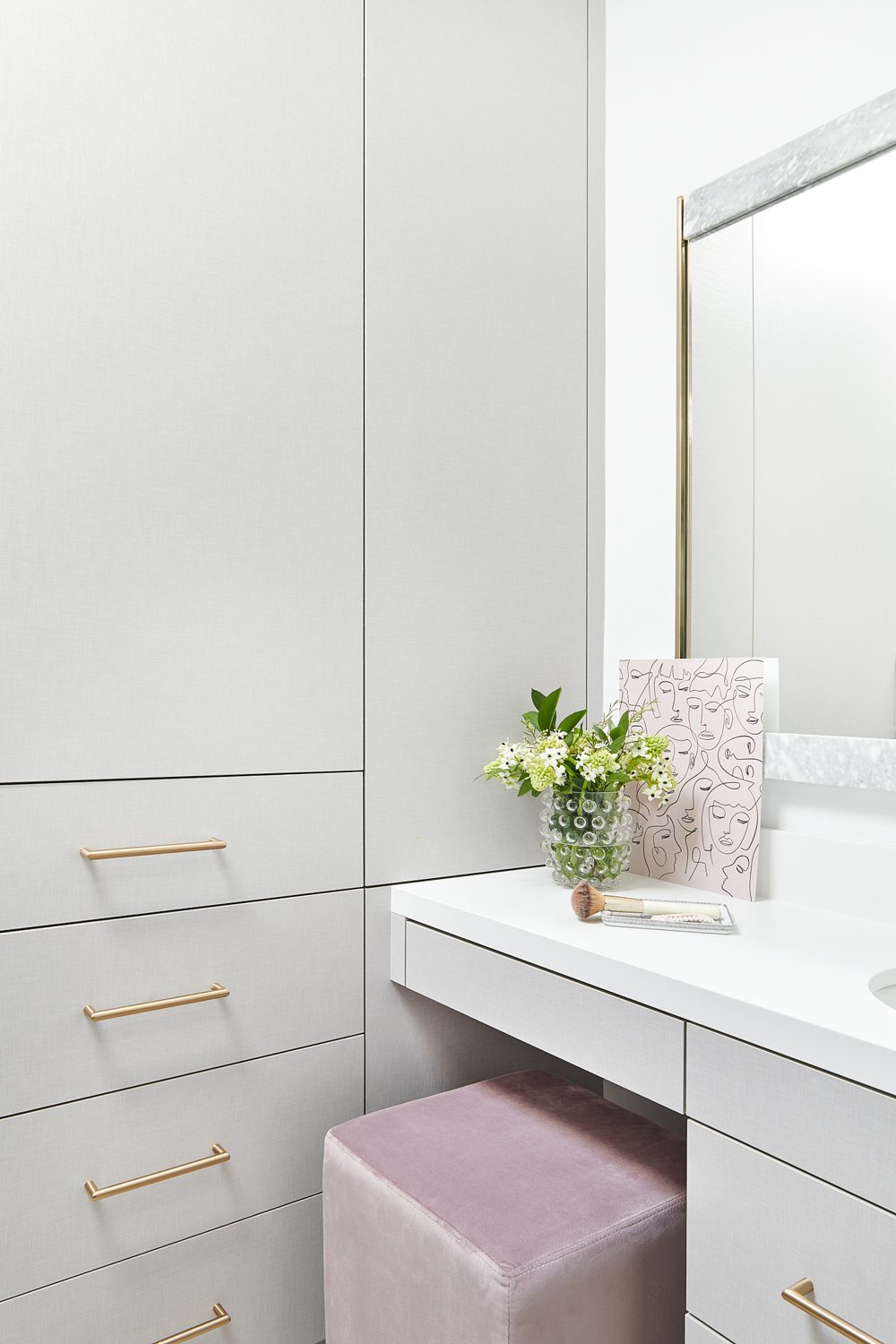 A white dressing table with brass pulls and a pink stool