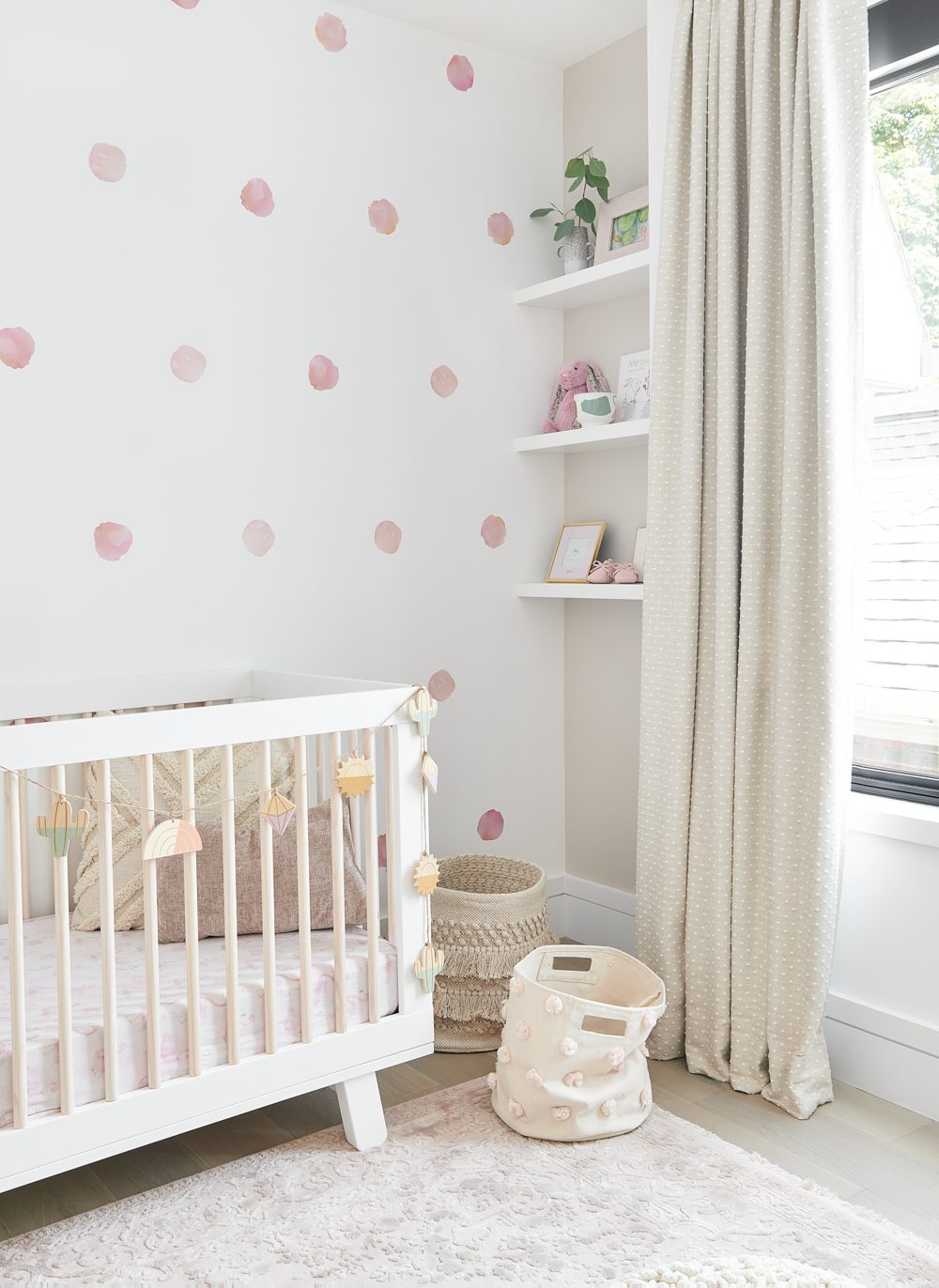 A nursery with a white crib and pink-dotted wallpaper