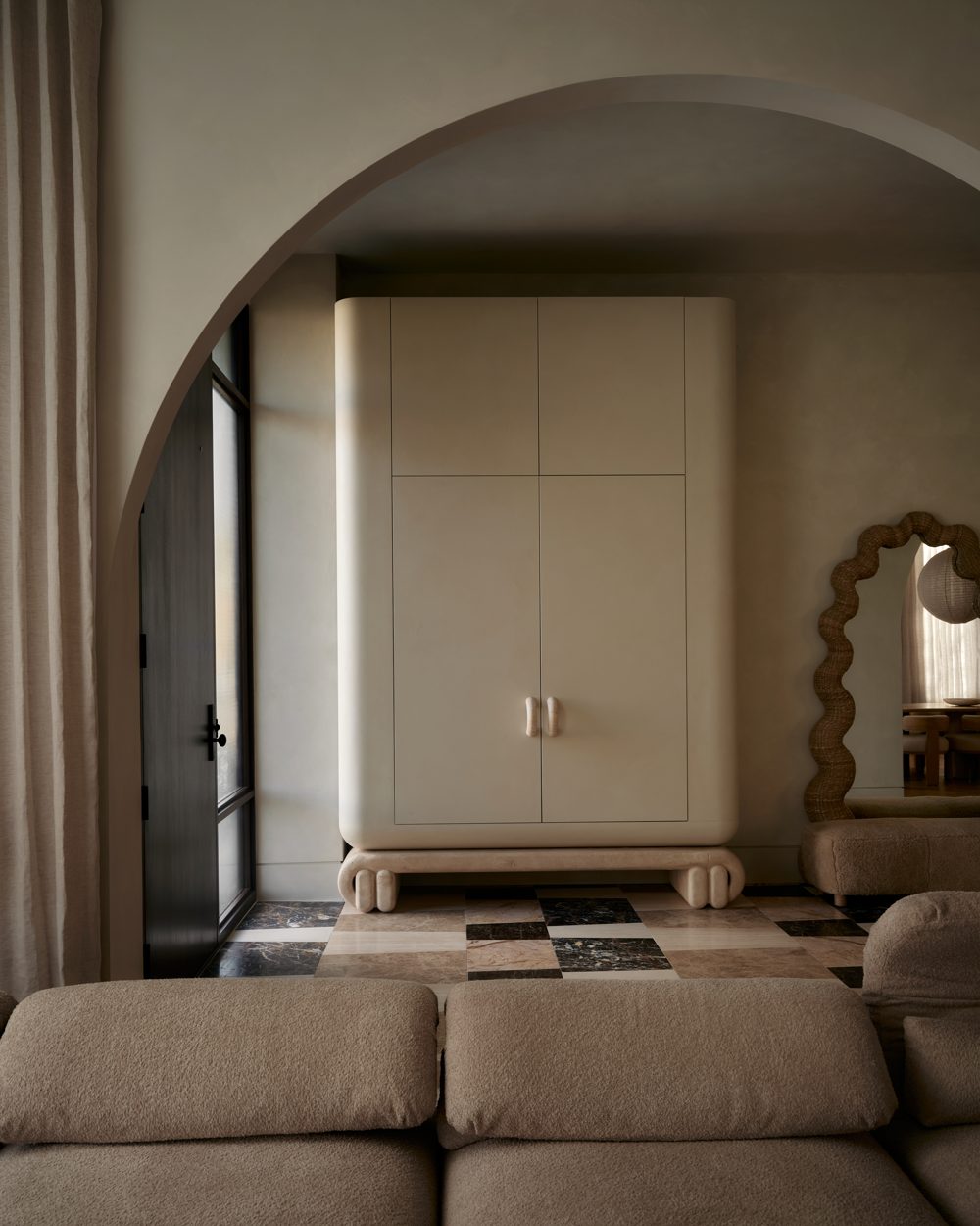 A plaster archway framing a cream lacquered wardrobe and a steel-framed front door