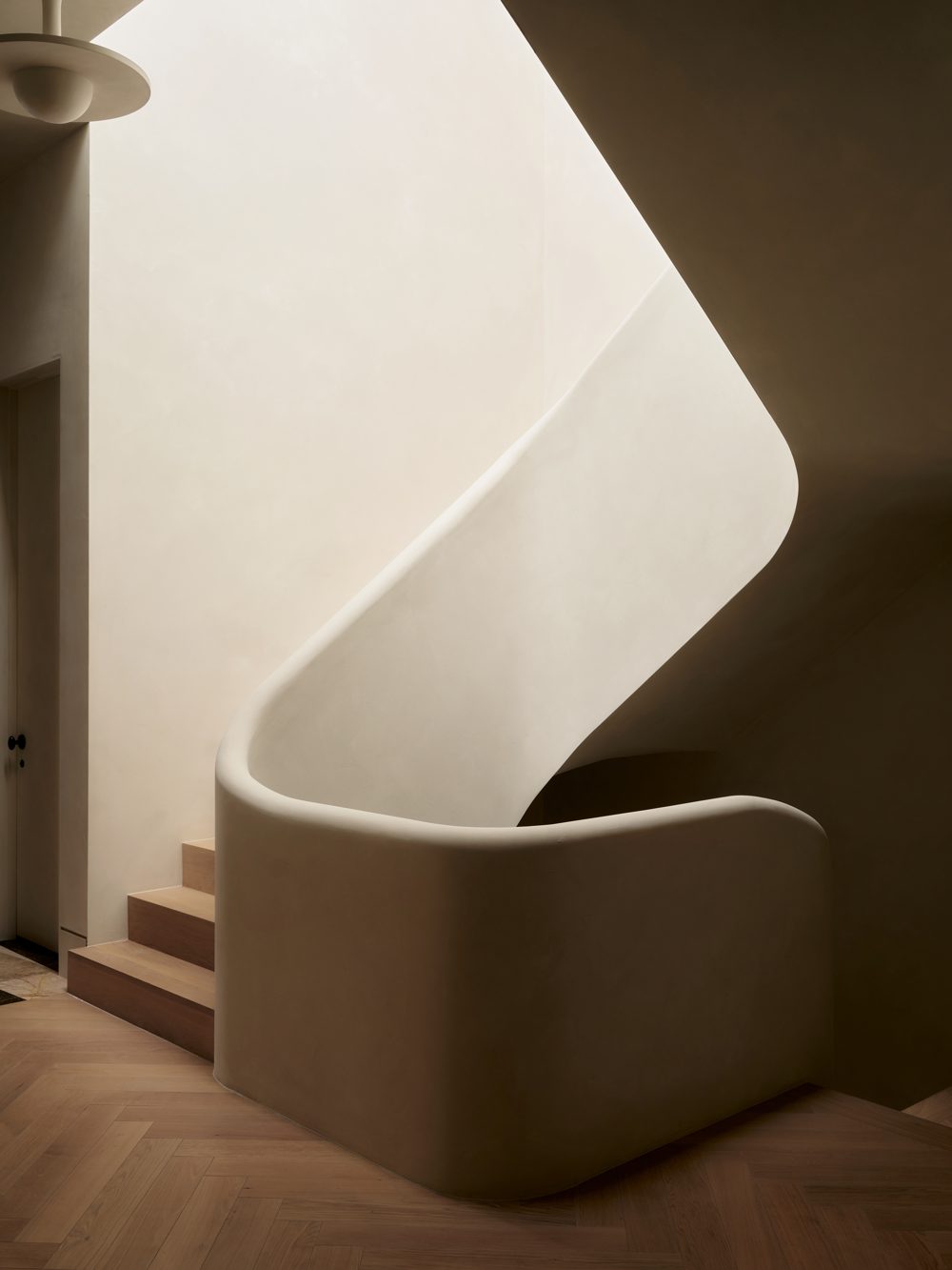 A curved plaster stair over a herringbone oak floor