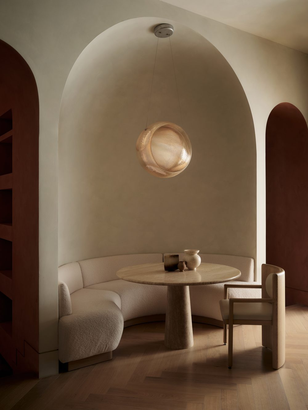 A curved boucle banquette in a plaster niche between two oxblood arches