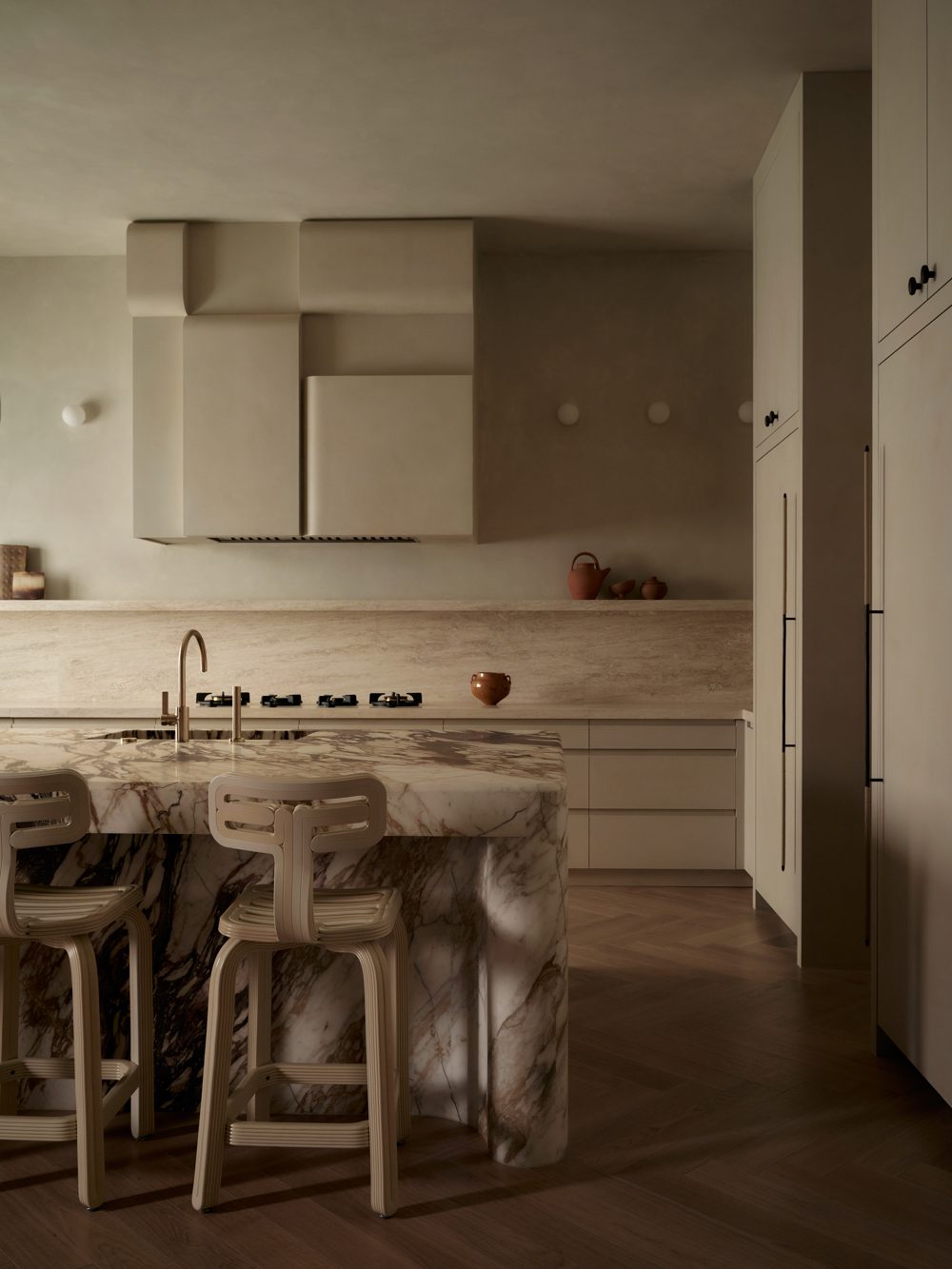 A marble island with heavy veining and sculpted wood stools