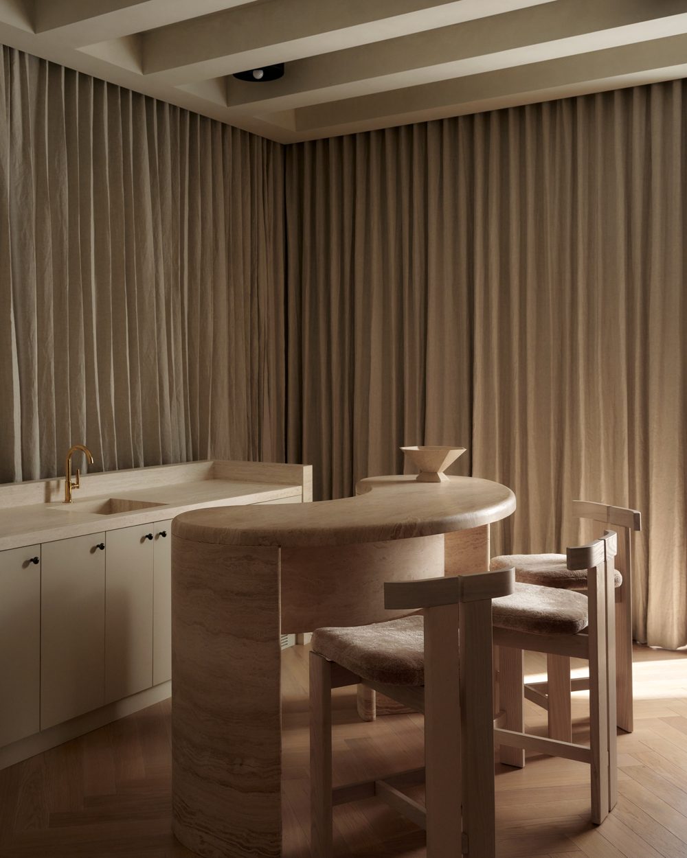 A pale oak dining table under a coffered ceiling, linen curtains on three walls