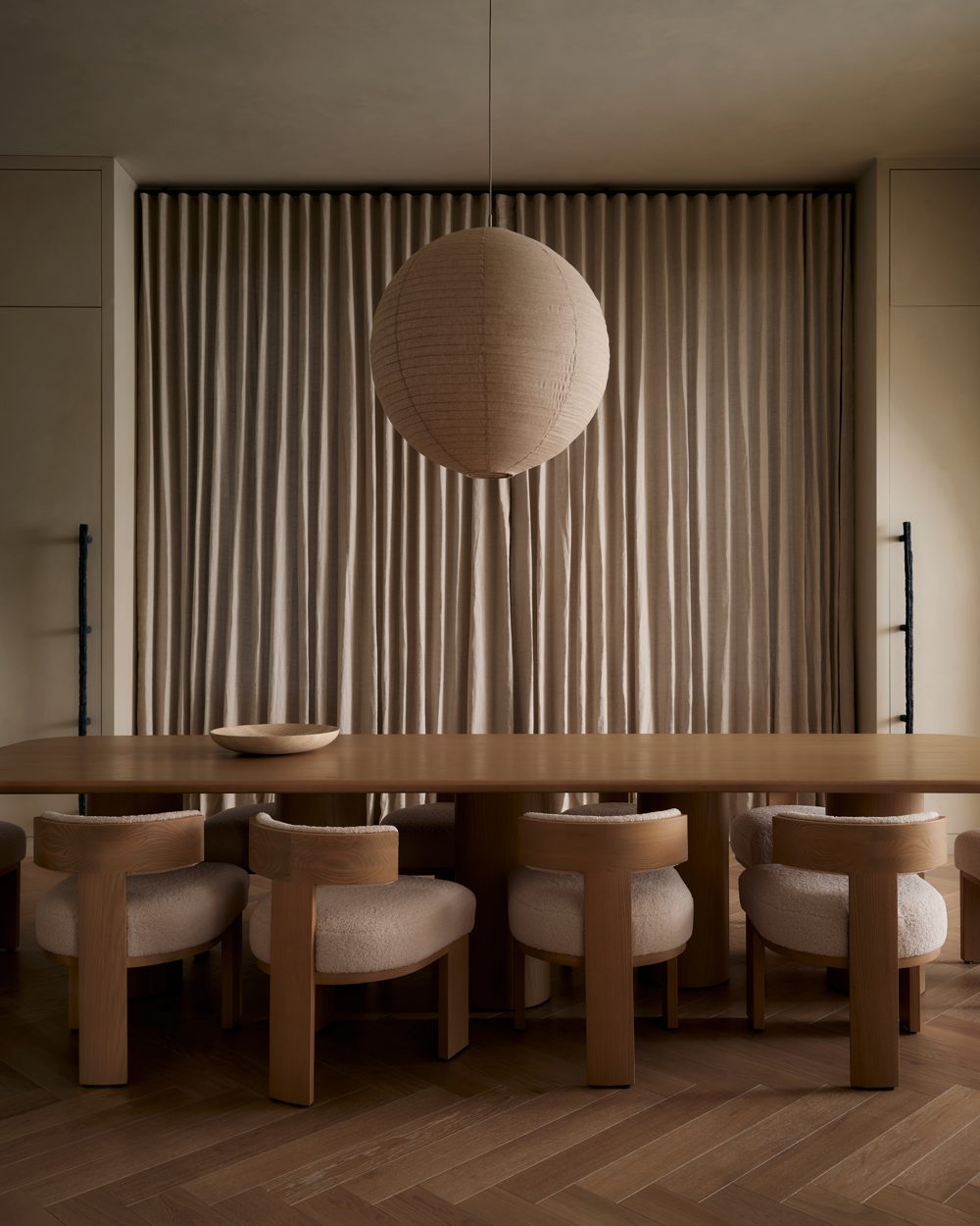 A long pale-oak table under a large linen globe pendant