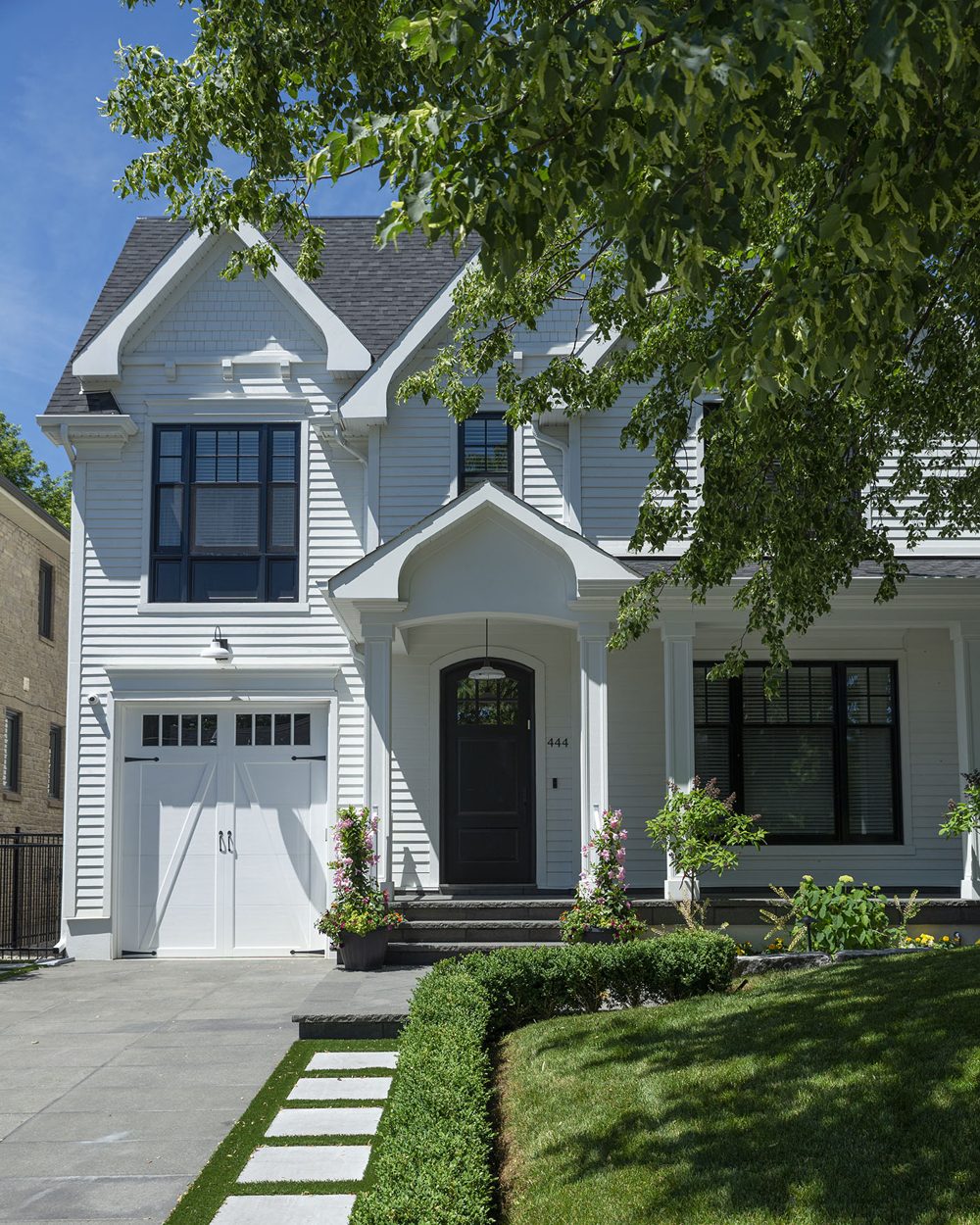 A white clapboard house with black windows, a gabled porch and a stone path