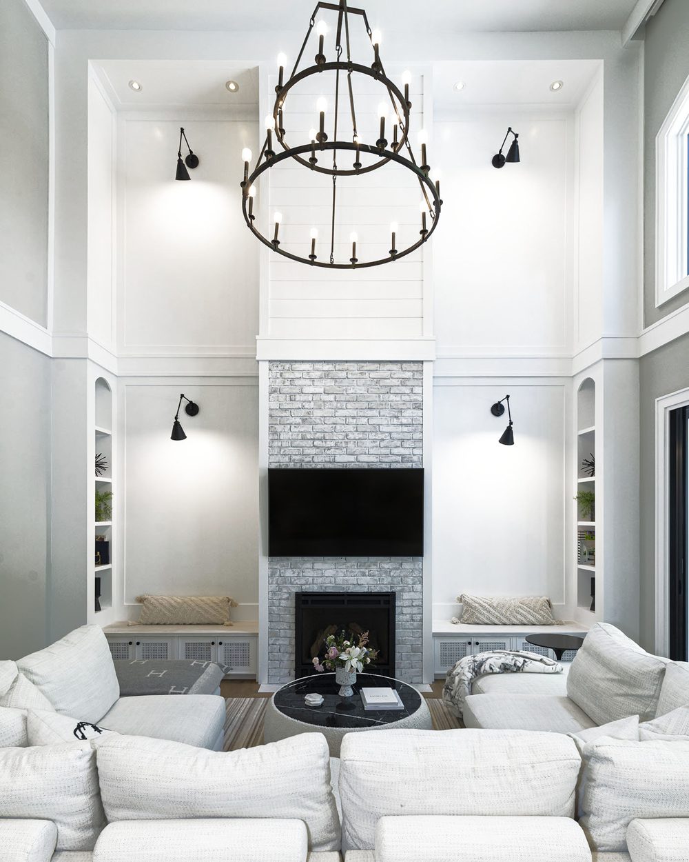 A double-height living room with a brick fireplace, a tiered iron chandelier and a white sectional