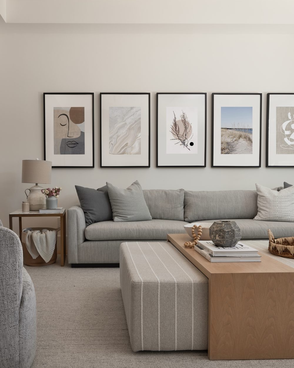 A grey sectional under five framed prints, with a striped ottoman and an oak coffee table