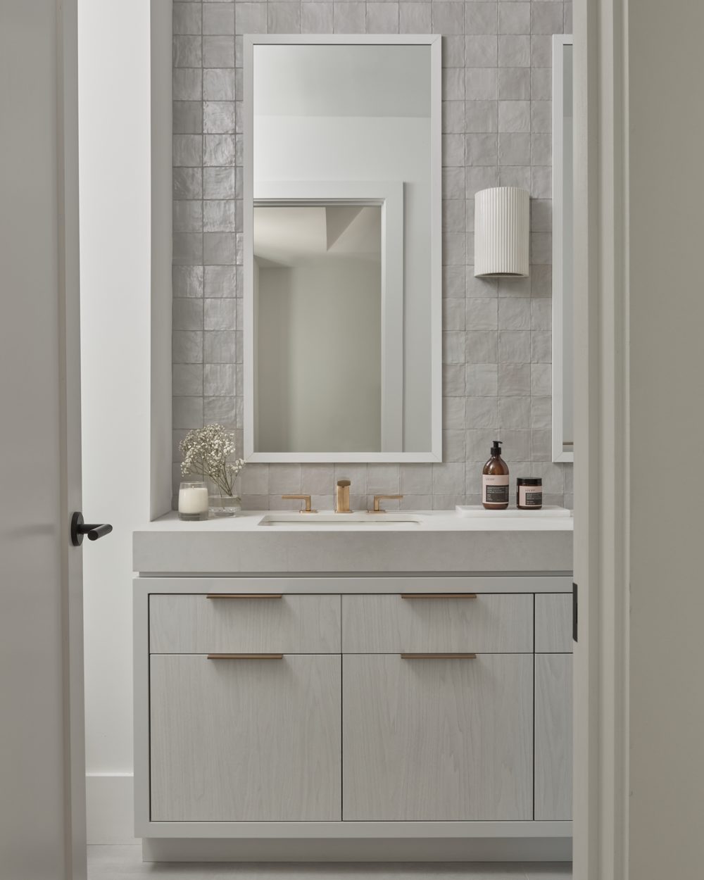 A powder room with grey zellige, a white vanity and brass taps