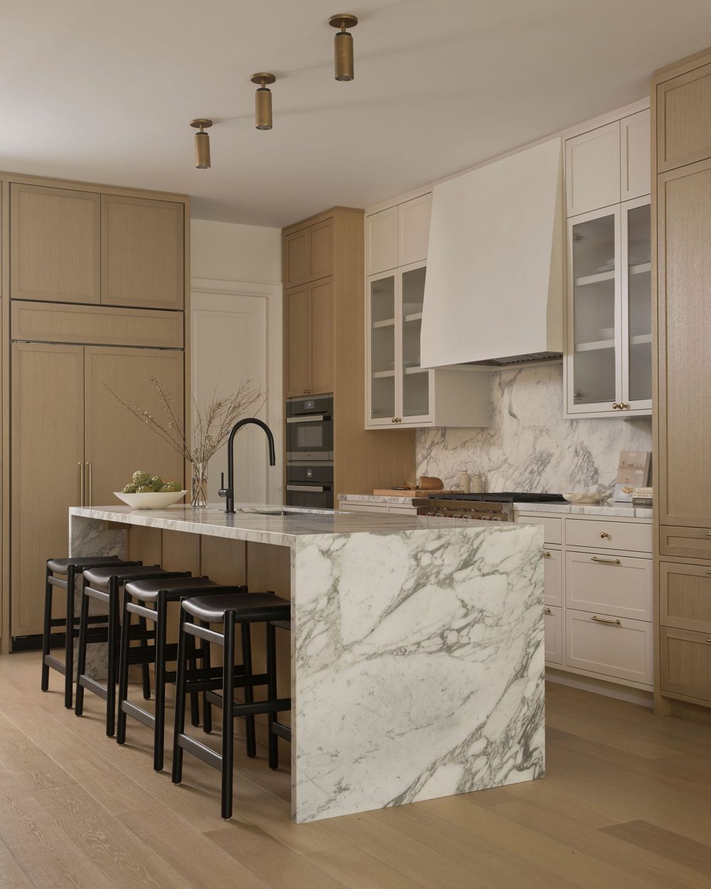 A marble waterfall island with black leather stools